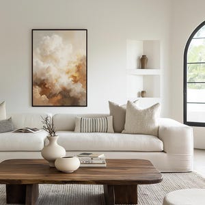 Può includere: Un soggiorno moderno con un grande dipinto astratto incorniciato, raffigurante forme simili a nuvole nei toni del marrone, beige e bianco. Un divano bianco è adornato da cuscini. Un tavolino in legno espone vasi e libri, creando un'atmosfera accogliente.