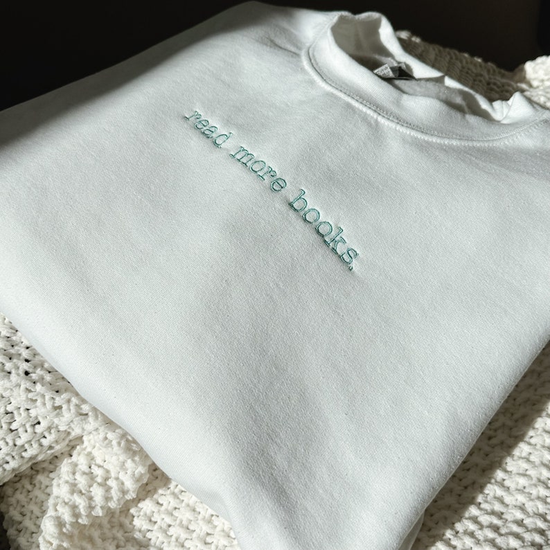 May include: White sweatshirt with the text "read more books" embroidered in teal.