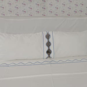 May include: White bed linens with light blue scalloped trim. The set includes a flat sheet, fitted sheet, and two pillowcases. The pillowcases have a vertical scalloped design in the center. The sheets are made of a smooth, soft fabric.