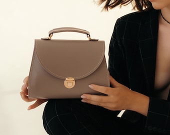 May include: A light brown leather satchel handbag with a gold clasp and a top handle.