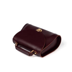 Elegant burgundy leather purse with curved flap and handle, shown from side angle.