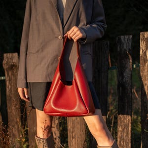 Red leather hobo bag held by woman in grey blazer outdoors