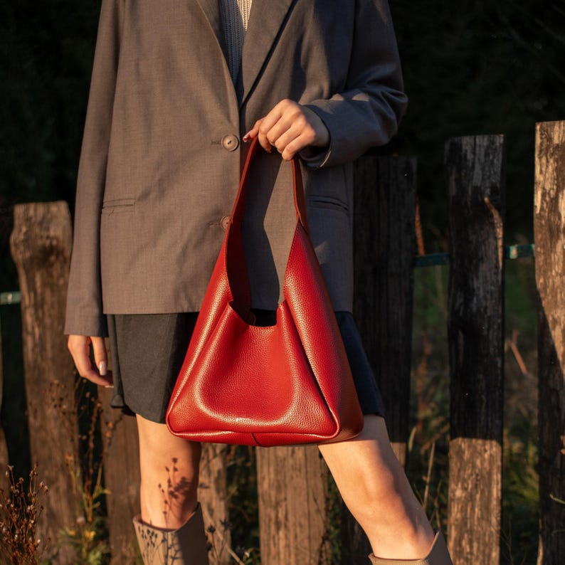 Red leather hobo bag held by woman in grey blazer outdoors