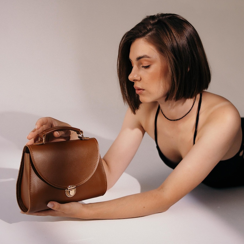 Woman in black outfit holding brown leather handbag with top handle.