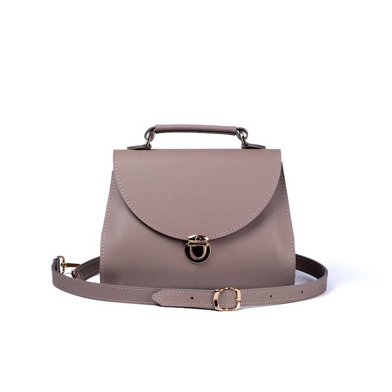 Gray leather crossbody bag with handle and gold push-lock clasp on white background.