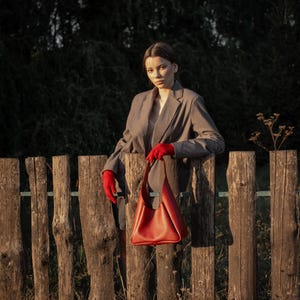 Woman standing by wooden fence holding red leather hobo bag
