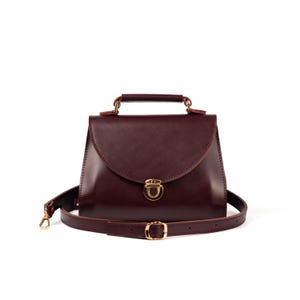 Burgundy leather top handle bag with gold clasp and detachable crossbody strap on white background.
