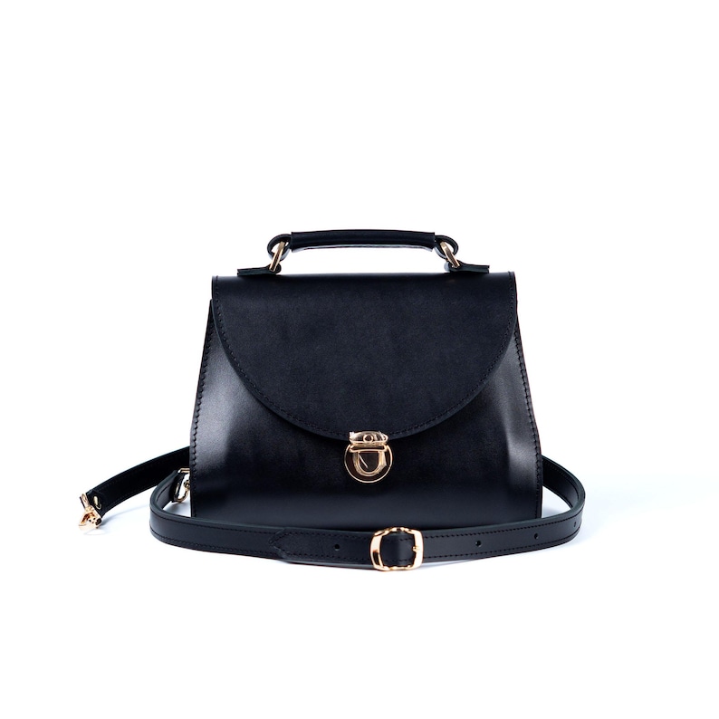 Black leather top handle bag with gold clasp and crossbody strap on white background.