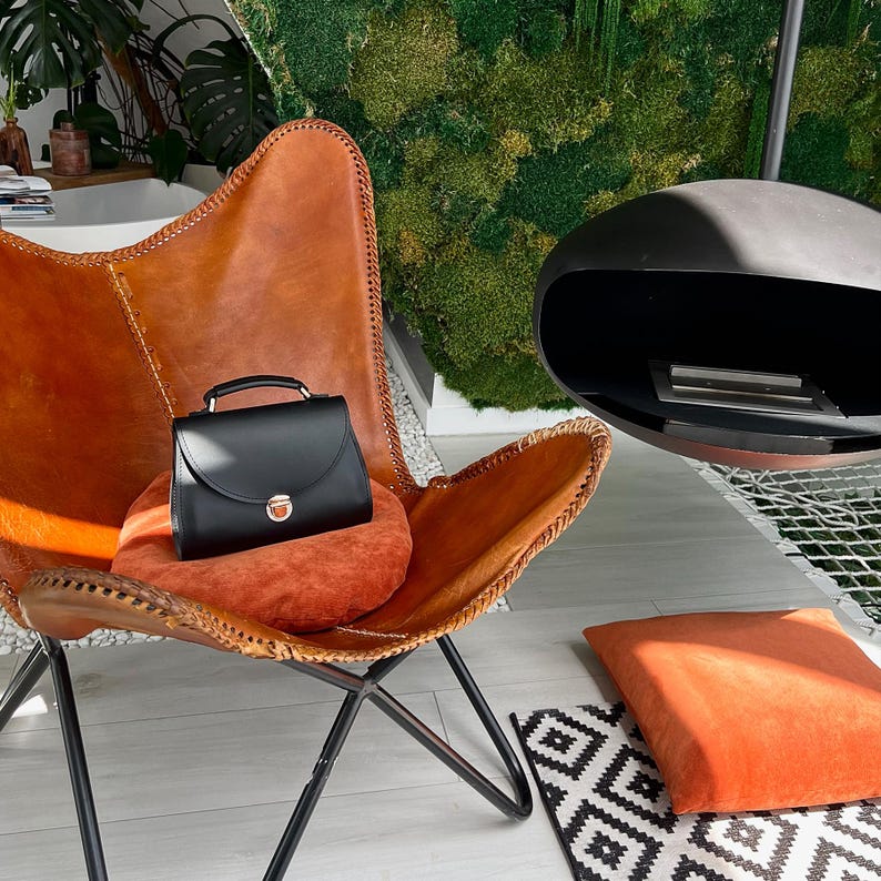 Black leather handbag with gold clasp resting on modern leather chair.