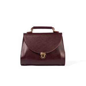 Structured burgundy leather handbag, minimalist design with rounded flap and metal lock.