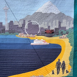 Może przedstawiać: Pikowana dekoracja ścienna przedstawiająca panoramę Seattle z iglicą Space Needle, ośnieżoną górą, diabelskim młynem i promem na niebieskiej wodzie. Żółta ścieżka ukazuje sylwetki dwóch osób i dwóch psów oraz znak Public Market Center.