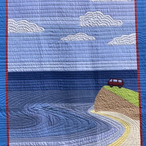 May include: A quilted wall hanging depicting a red van parked on a cliff overlooking a blue ocean with a winding road leading to the van. The sky is blue with white clouds.