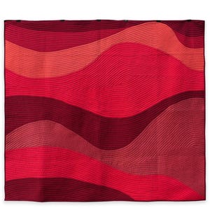 May include: A quilted blanket with a wavy design in shades of red. The blanket features a variety of red hues, from deep burgundy to bright coral. The stitching creates a textured, rippled effect across the surface.