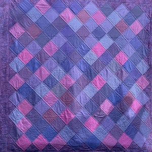 May include: A quilt made of various shades of purple and pink fabric, with a diamond pattern.
