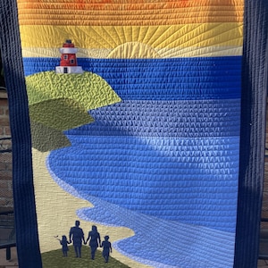 Peut inclure: Une tenture murale matelassée représentant un paysage marin avec un phare sur une colline verte, une mer bleue et une famille de quatre personnes se promenant sur une plage de sable au coucher du soleil. Le ciel est un dégradé d'orange, de jaune et de blanc.