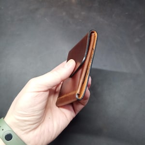 May include: A brown leather wallet with a fold-over flap and a black stitched edge.