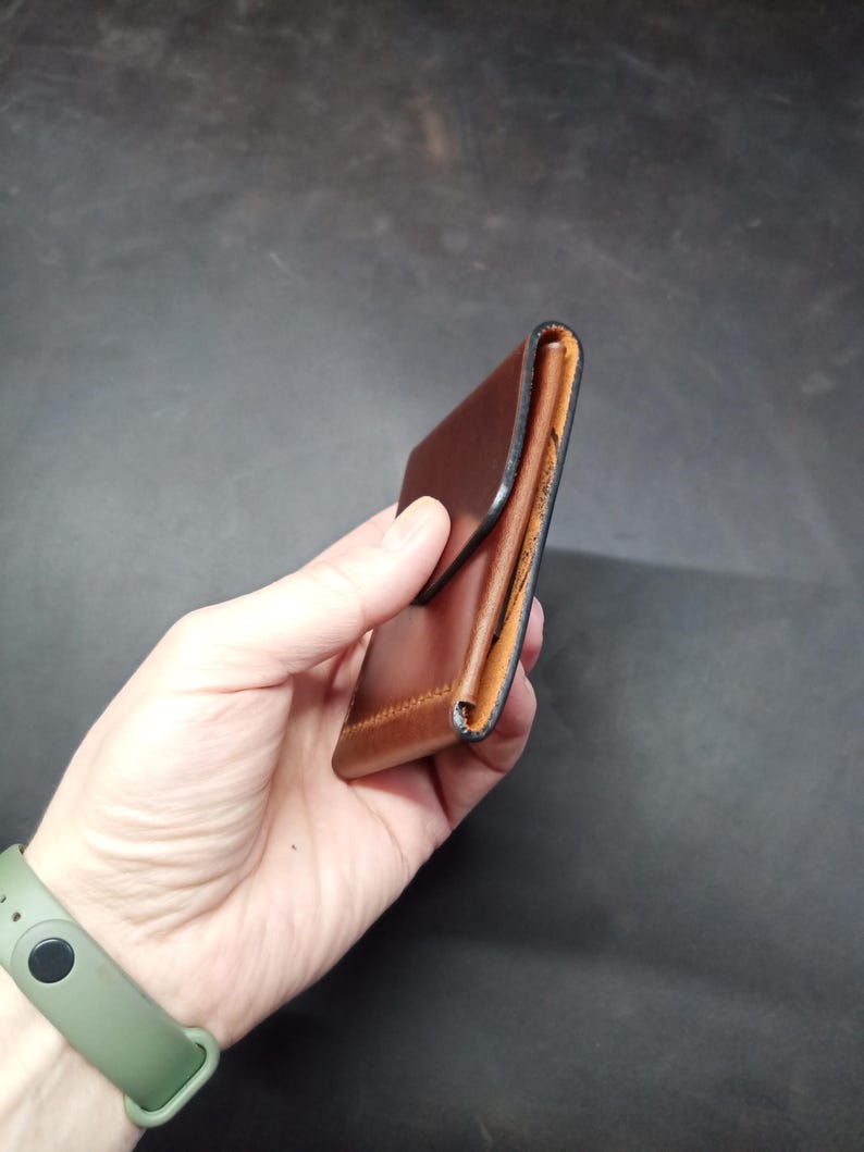 May include: A brown leather wallet with a fold-over flap and a black stitched edge.