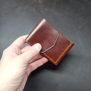 May include: A brown leather wallet with a flap closure. The wallet is folded in half and has a stitched edge.