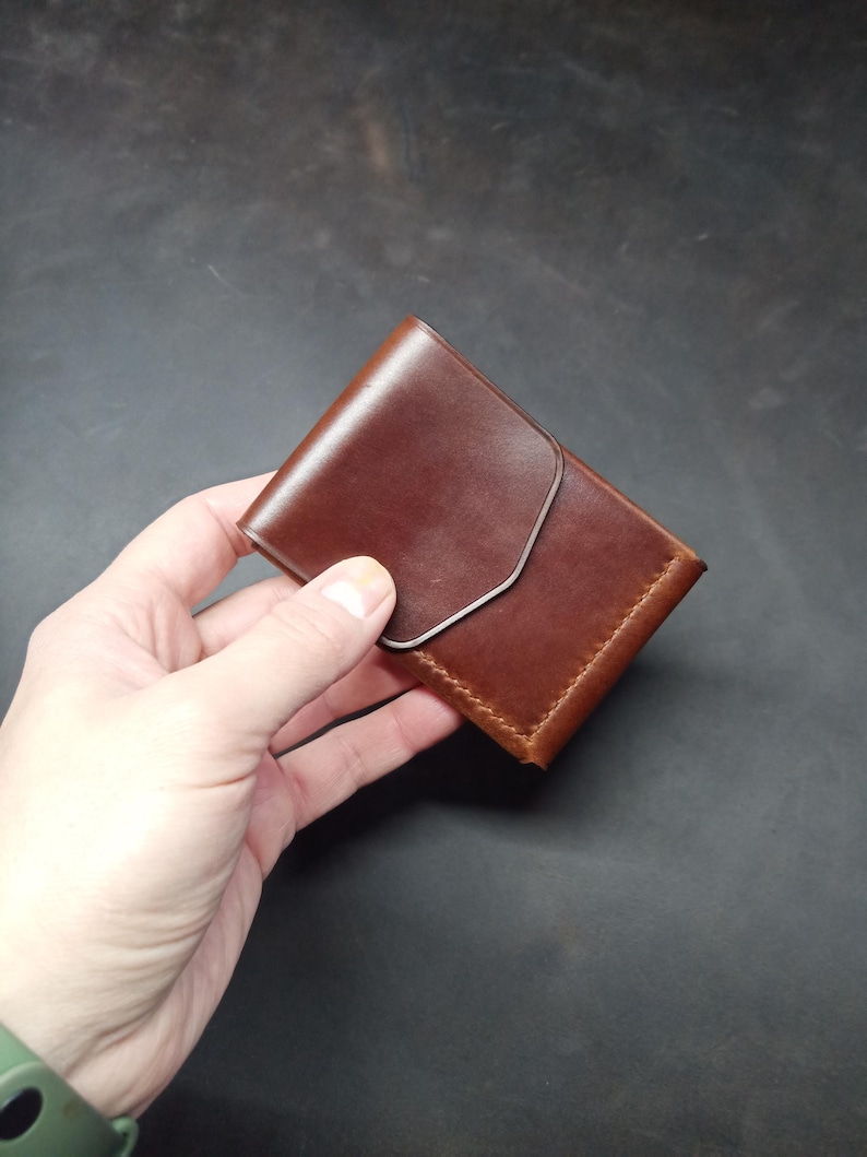 May include: A brown leather wallet with a flap closure. The wallet is folded in half and has a stitched edge.