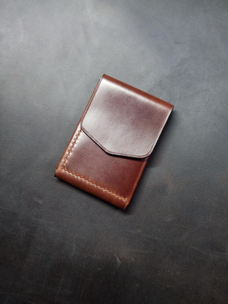 May include: A brown leather wallet with a flap closure. The wallet has a stitched edge and a smooth finish.