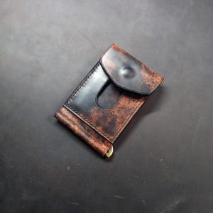 May include: A brown leather wallet with a money clip and a flap closure. The wallet has a distressed look and is made of high-quality leather.