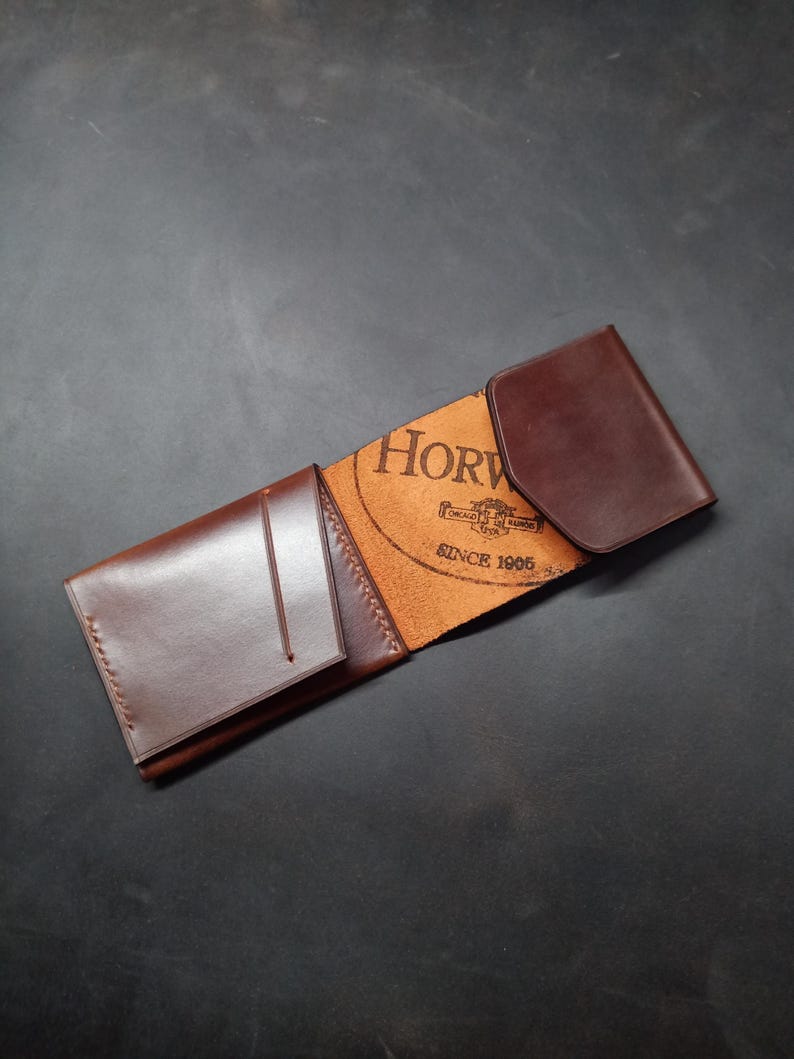 May include: A brown leather wallet with a fold-over flap. The wallet has a small pocket on the front and the Horween Leather Company logo is embossed on the inside.