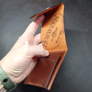 May include: A brown leather wallet with a Horween leather label. The label is orange and has the text "Horween" and "Since 1905" in black.