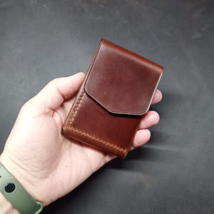 May include: A brown leather wallet with a flap closure. The wallet is held in a hand.