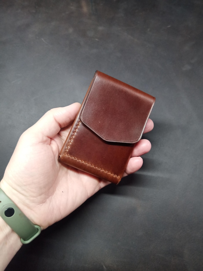 May include: A brown leather wallet with a flap closure. The wallet is held in a hand.