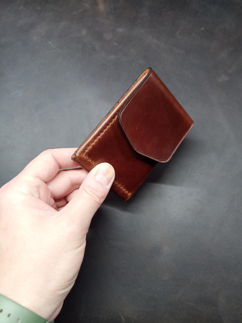 May include: A brown leather wallet with a flap closure. The wallet is held in a hand.
