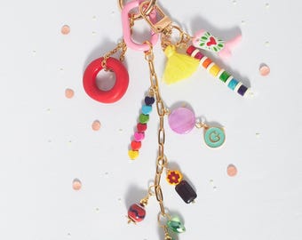 May include: A colorful keychain with multiple charms. The keychain features a gold-tone clasp and a pink ring. Charms include a red donut, a rainbow-colored beaded chain, a yellow tassel, and a strawberry charm. Other charms include a purple circle and a green circle with a "G".