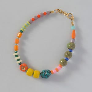 Puede incluir: Una colorida pulsera de cuentas con un cierre dorado. La pulsera presenta una variedad de cuentas en naranja, amarillo, verde, azul, rosa y morado. Las cuentas son de varias formas y tamaños, incluyendo redondas, cuadradas y florales.