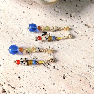 May include: A pair of dangle earrings with a gold post and chain. Each earring features a large blue bead, followed by a series of smaller beads in various colors, including orange, green, and white. The earrings are approximately 2 inches long.
