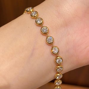 Puede incluir: Una pulsera de cadena dorada que presenta una serie de piedras transparentes redondas engastadas en bisel. La pulsera consta de m&uacute;ltiples engastes circulares dorados, cada uno con una piedra facetada y brillante dispuesta en l&iacute;nea.
