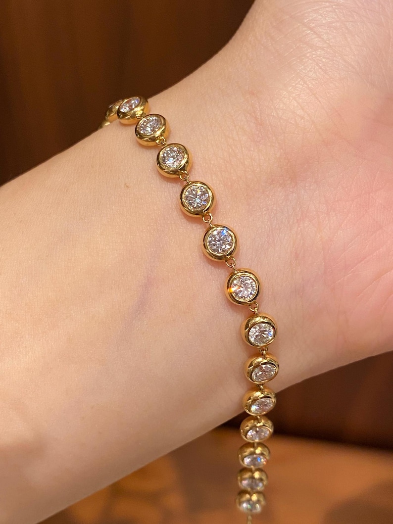 Puede incluir: Una pulsera de cadena dorada que presenta una serie de piedras transparentes redondas engastadas en bisel. La pulsera consta de m&uacute;ltiples engastes circulares dorados, cada uno con una piedra facetada y brillante dispuesta en l&iacute;nea.
