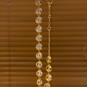 Puede incluir: Una pulsera de cadena dorada que presenta una serie de piedras claras redondas engastadas en bisel. La pulsera incluye una secci&oacute;n de cadena de eslabones delicados con un cierre circular, con un acabado en oro amarillo pulido y piedras facetadas.
