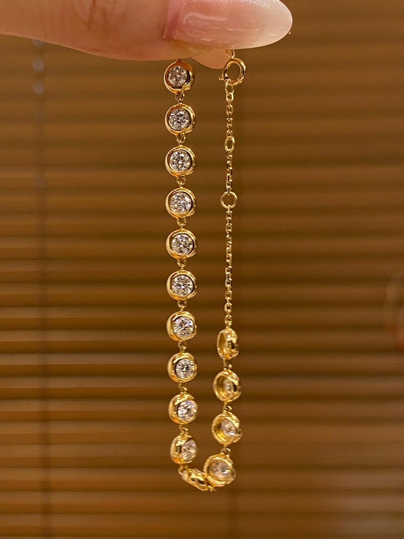 Puede incluir: Una pulsera de cadena dorada que presenta una serie de piedras claras redondas engastadas en bisel. La pulsera incluye una secci&oacute;n de cadena de eslabones delicados con un cierre circular, con un acabado en oro amarillo pulido y piedras facetadas.