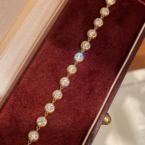 Puede incluir: Una pulsera de cadena dorada que presenta una serie de piedras transparentes redondas engastadas en bisel. Cada piedra est&aacute; encerrada en un engaste circular de oro pulido, conectado por peque&ntilde;os eslabones dorados, creando una l&iacute;nea continua de acentos circulares.