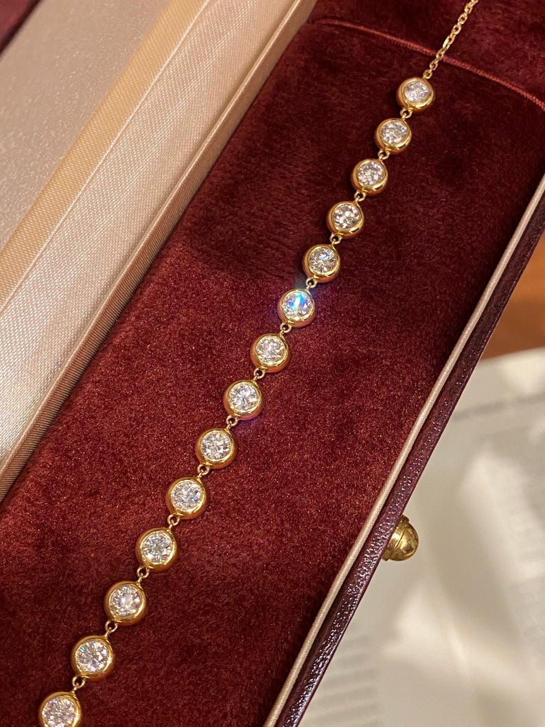 Puede incluir: Una pulsera de cadena dorada que presenta una serie de piedras transparentes redondas engastadas en bisel. Cada piedra est&aacute; encerrada en un engaste circular de oro pulido, conectado por peque&ntilde;os eslabones dorados, creando una l&iacute;nea continua de acentos circulares.