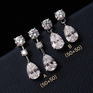 Puede incluir: Pendientes de plata con piedras preciosas claras y brillantes. Cada pendiente presenta una piedra redonda en la parte superior, una piedra de acento más pequeña y una gran gota en forma de pera. El texto "A (50+50)" y "B (50+50)" es visible.