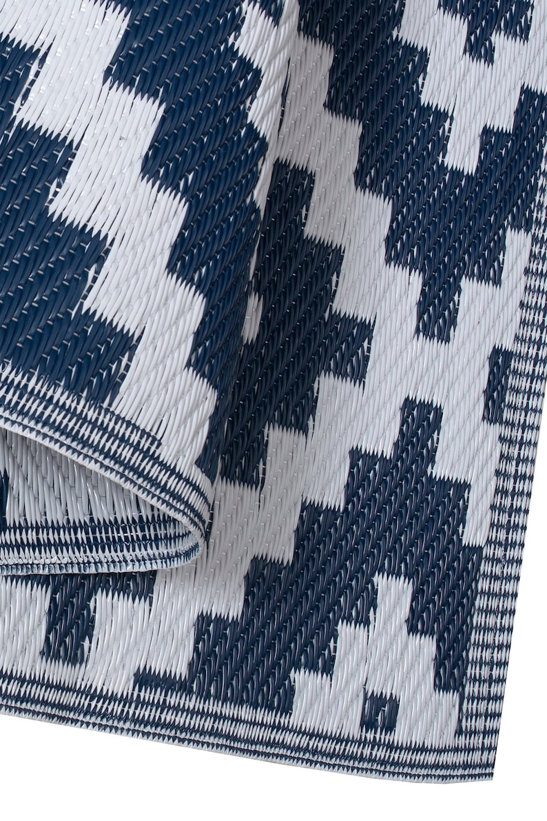 May include: A close-up of a blue and white checkered outdoor rug. The rug is made of woven plastic and has a textured surface.