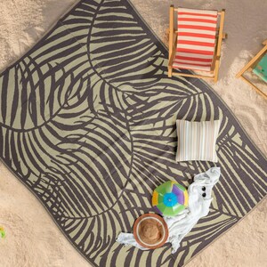 May include: A brown and beige beach blanket with a zebra-like pattern. The blanket is laid out on a sandy beach with two striped beach chairs and a beach shovel.