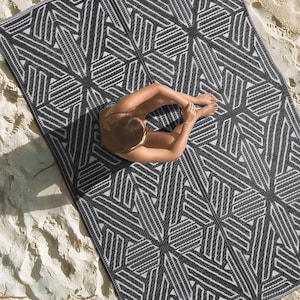 Pode incluir: Um tapete de exterior geom&eacute;trico preto e branco com uma pessoa sentada nele. O tapete &eacute; feito de um material tecido e tem um design moderno.