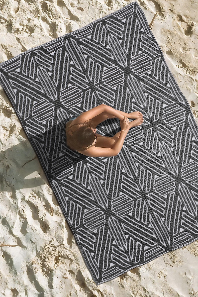 Pode incluir: Um tapete de exterior geom&eacute;trico preto e branco com uma pessoa sentada nele. O tapete &eacute; feito de um material tecido e tem um design moderno.