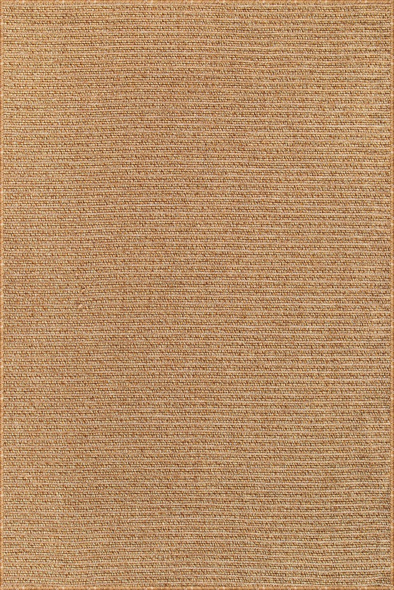 May include: A rectangular, woven rug in a natural tan color. The rug has a textured surface with a repeating horizontal pattern. The edges are finished with a darker border.