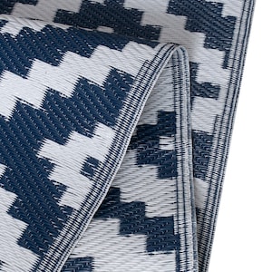 May include: A blue and white patterned outdoor rug made of woven plastic. The rug is folded in half and the edges are visible.