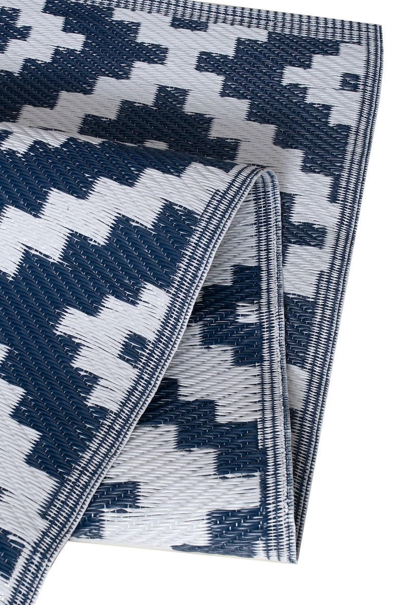 May include: A blue and white patterned outdoor rug made of woven plastic. The rug is folded in half and the edges are visible.