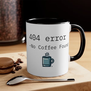 May include: White ceramic coffee mug with a black rim and handle. The mug has a black and white graphic that says "404 error -No Coffee Found" with a small icon of a steaming coffee cup.