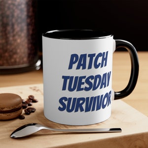 May include: White ceramic coffee mug with a black rim and handle. The mug has the text "PATCH TUESDAY SURVIVOR" printed in blue.