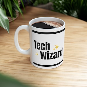May include: White ceramic mug with a black border and the text "Tech Wizard" in black with gold stars. The mug is filled with coffee.